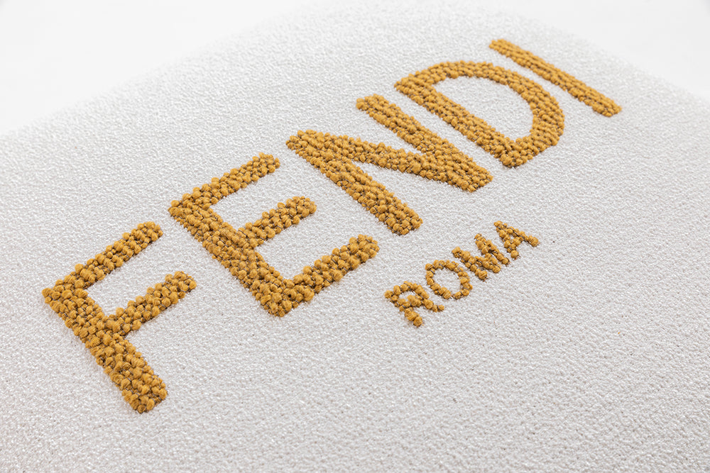 Detail of Fendi Roma logo embroidery on luxury bouclé cushion, iconic design element for furniture Fendi Casa